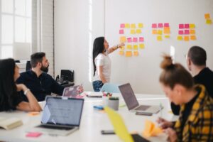 A manager presents on a whiteboard to a room full of employees at a conference table.